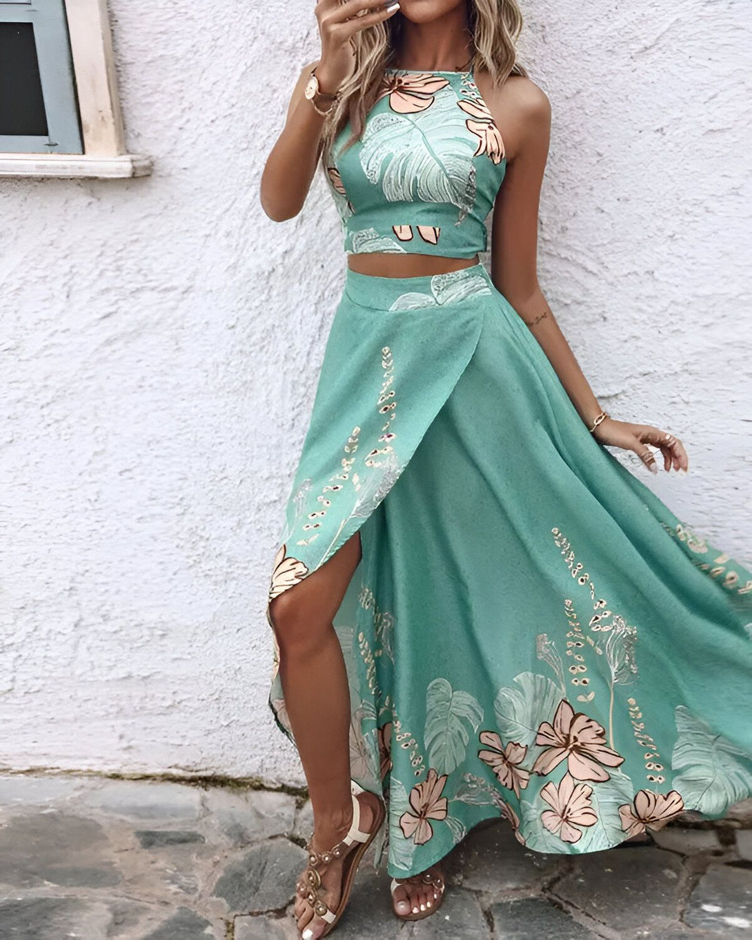 Une femme porte un ensemble deux pièces vert avec un motif de feuilles et de fleurs. Le haut est un crop top et la jupe est longue et fendue sur le côté.