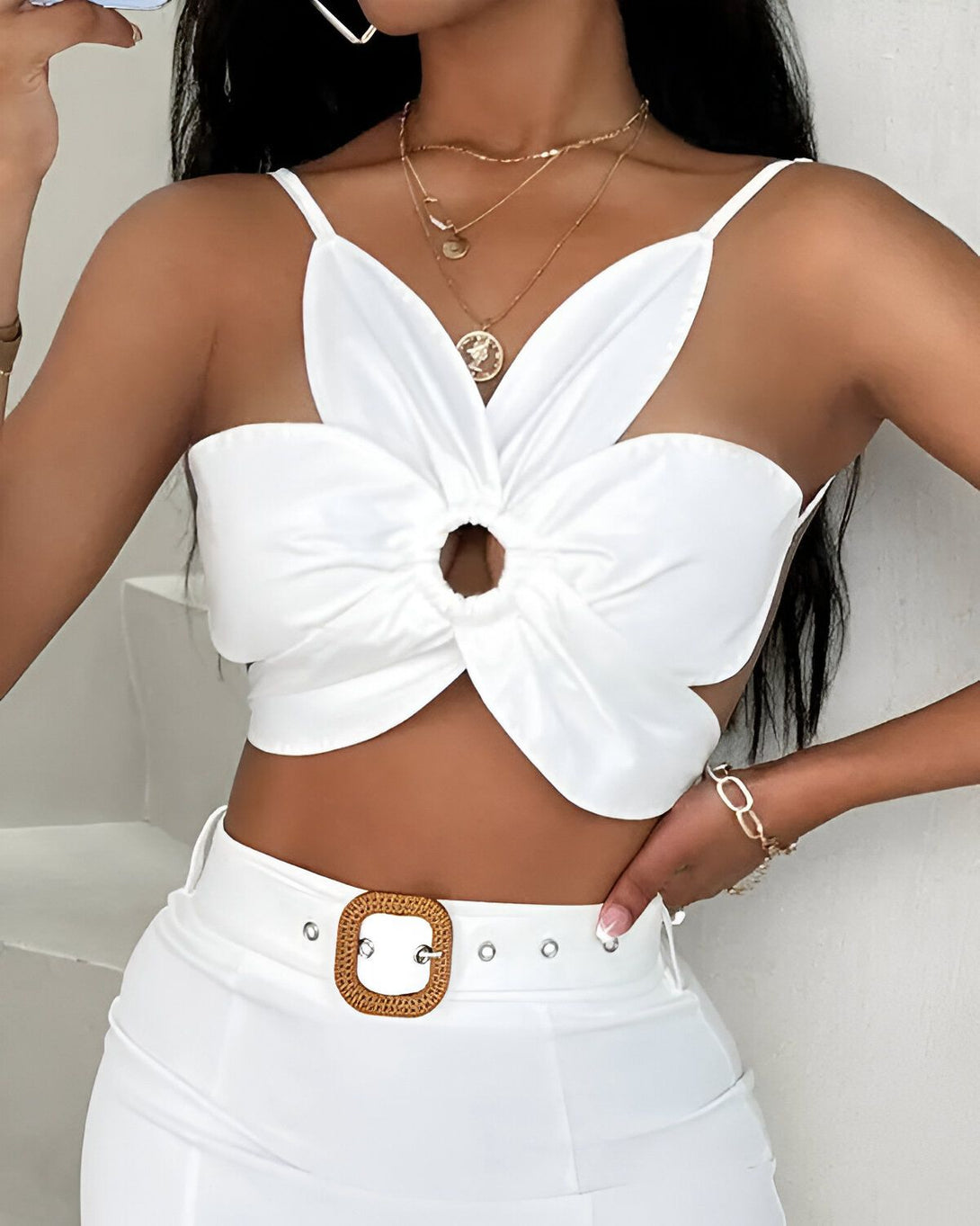 Une jeune femme porte un haut court blanc avec un trou en forme de fleur au centre. Elle porte également un pantalon blanc et une ceinture marron.