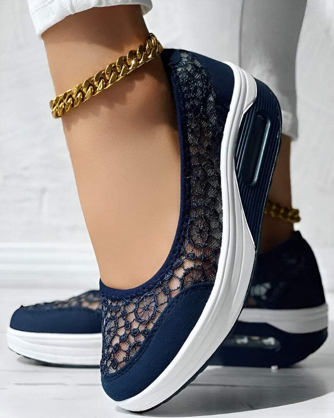 Une femme porte des chaussures bleues en dentelle avec une semelle blanche. Elle porte également un pantalon blanc et un bracelet de cheville doré.