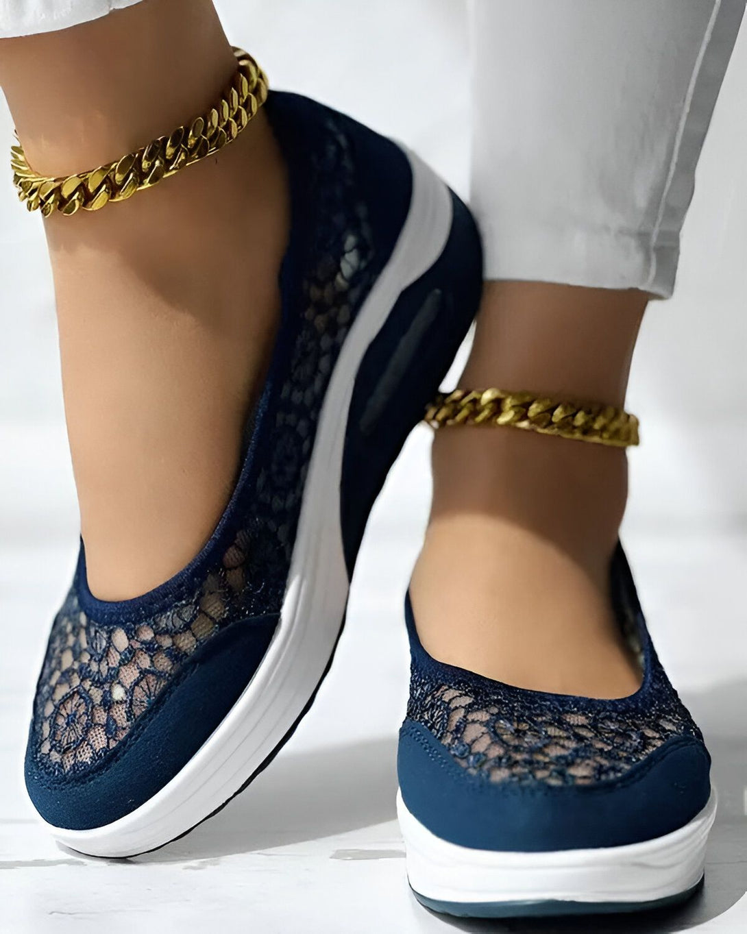 Une femme porte des chaussures bleues en dentelle avec des semelles blanches. Elle porte également des bracelets de cheville en or.