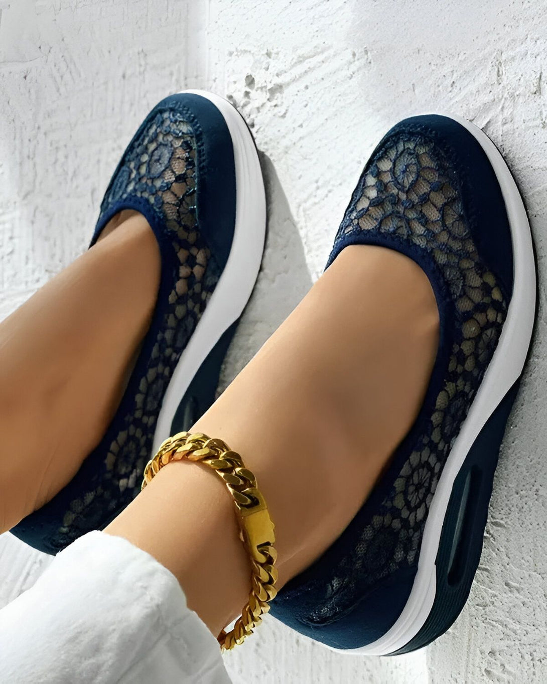 Une femme porte des chaussures bleues en dentelle avec une semelle blanche. Elle porte également un pantalon blanc et un bracelet doré à la cheville.