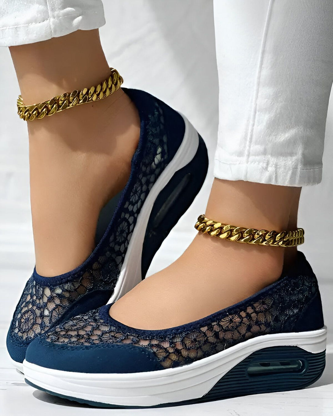 Une femme porte des chaussures bleues en dentelle avec des semelles blanches et des chaînes dorées aux chevilles.