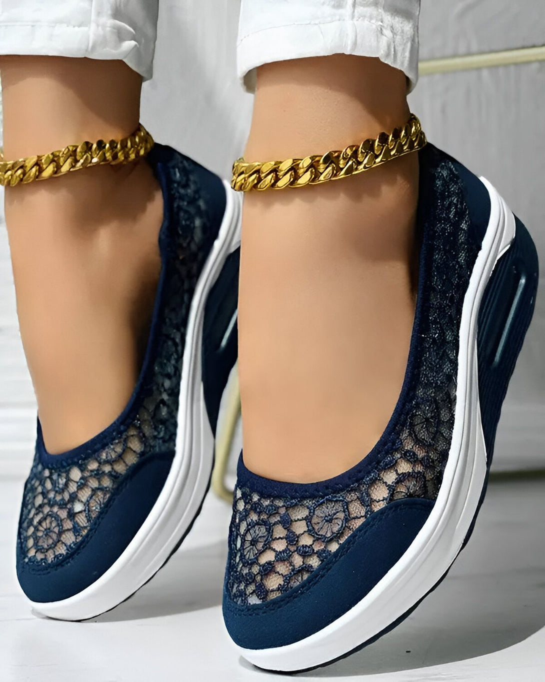 Une femme porte des chaussures bleues en dentelle avec un talon compensé blanc. Elle porte également une chaîne dorée autour de la cheville.