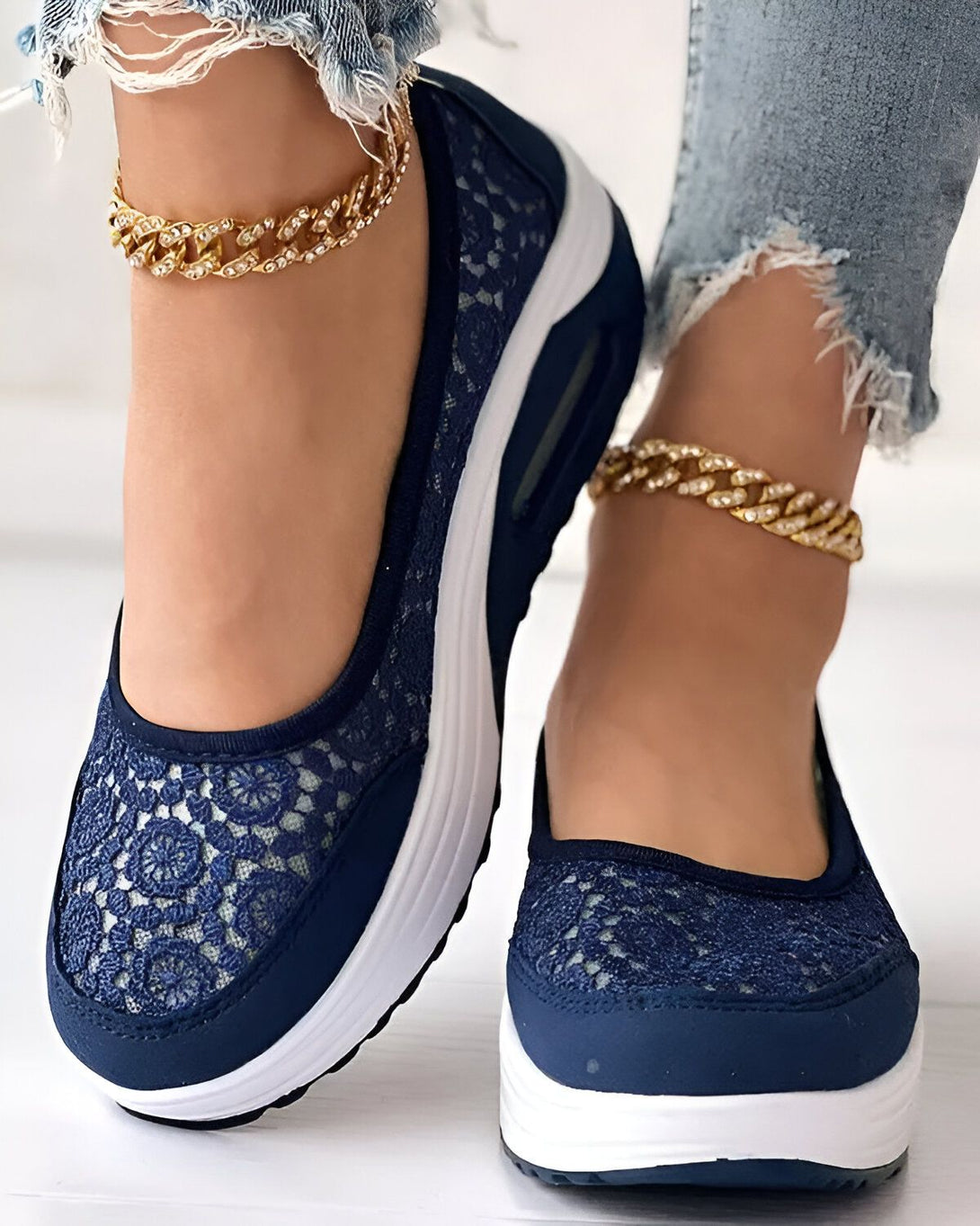 Une femme porte des baskets bleues en dentelle avec une semelle blanche. Elle porte également un jean et des bijoux.