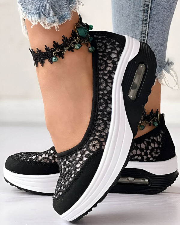 Une femme porte des chaussures noires en dentelle avec des semelles blanches. Elle porte également un bracelet de cheville en dentelle noire avec des perles vertes.