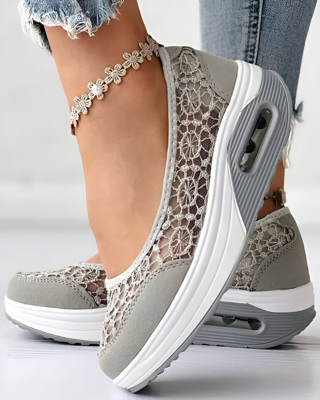 Une femme porte des baskets grises en dentelle avec une semelle blanche. Les baskets sont légères et respirantes, idéales pour le printemps et l'été.