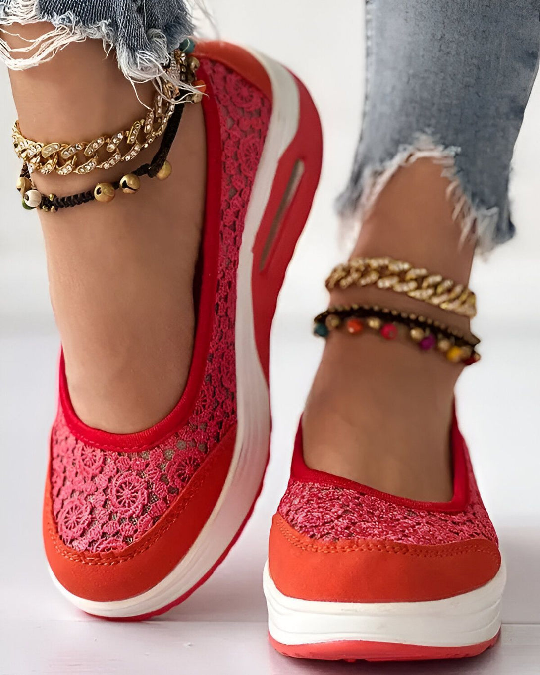 Une femme porte des baskets rouges en dentelle avec une semelle blanche. Elle porte également des jeans troués et des bracelets de cheville.