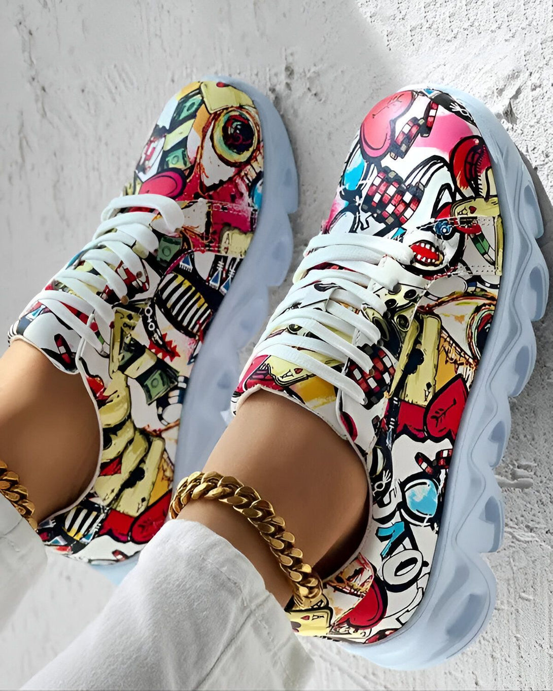 Une paire de baskets multicolores avec des lacets blancs et une semelle épaisse blanche. Les baskets sont portées par une femme qui porte un jean et un t-shirt blanc. La femme est assise sur un banc et elle a les pieds croisés.