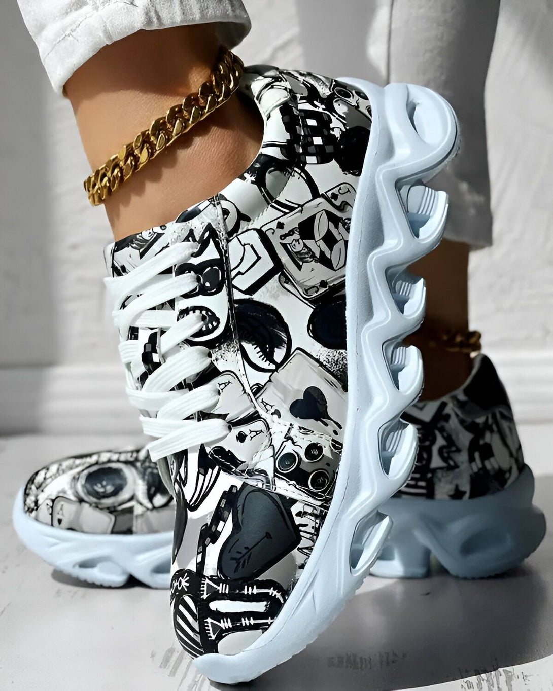 Une paire de baskets montantes noires et blanches à lacets avec une semelle épaisse et crantée. Les baskets sont portées par une femme qui porte un jean et un t-shirt blancs. La femme est debout sur un sol en béton.