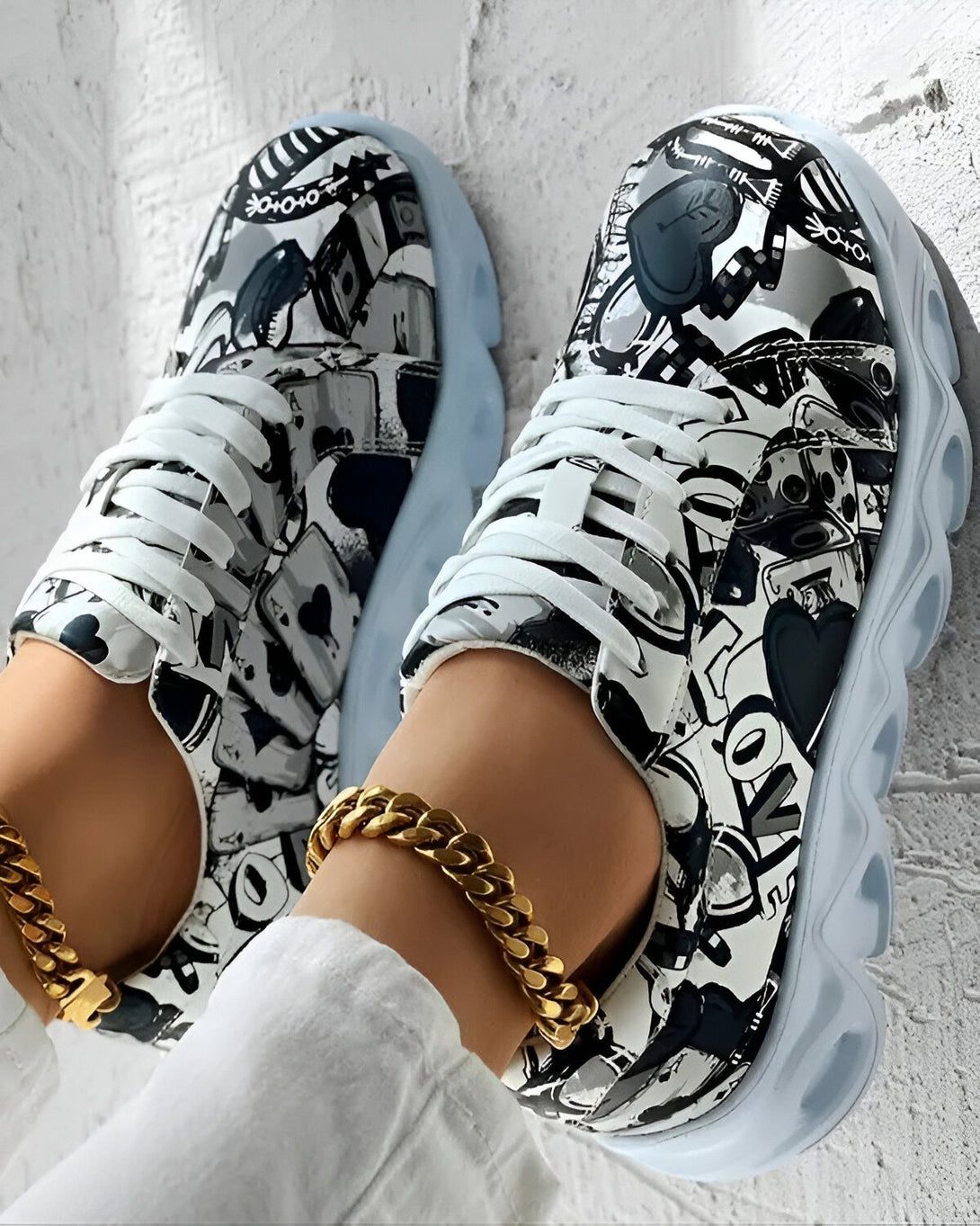 Une paire de baskets montantes noires et blanches avec des motifs de cœurs, de trèfles, de piques et de carreaux. Les baskets sont portées par une femme qui porte également un bracelet de cheville doré.