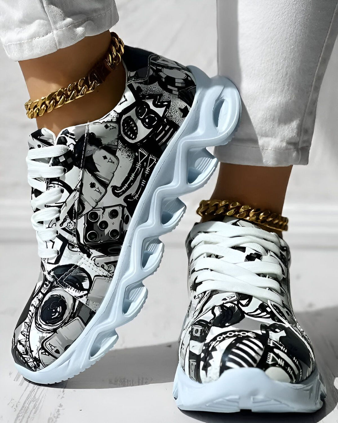 Une paire de baskets montantes à lacets, noires et blanches, avec une semelle épaisse et crantée. Les baskets sont portées par une femme qui porte un jean blanc et un haut noir.