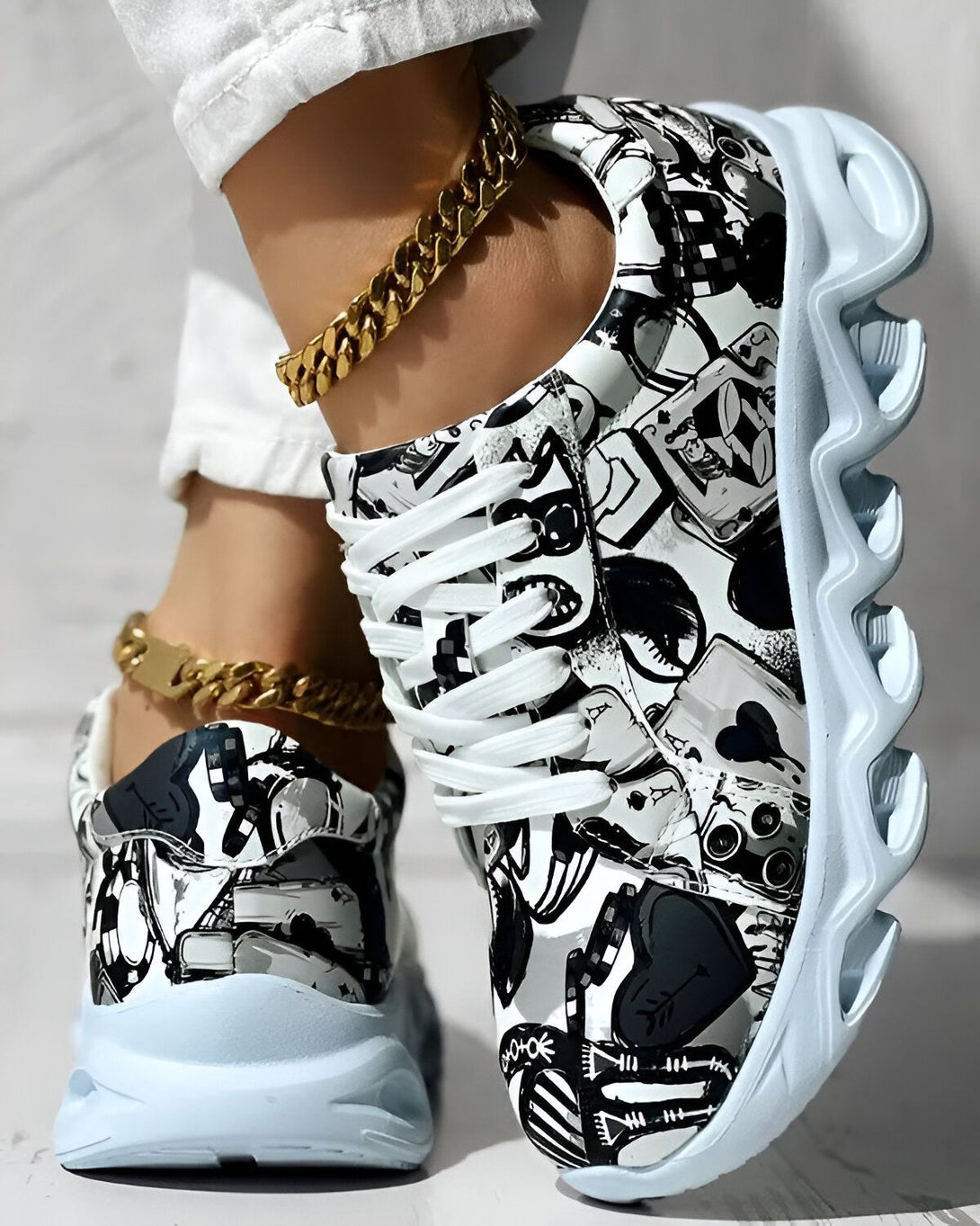 Une paire de baskets noires et blanches avec un motif de cartes à jouer. Les baskets sont portées par une femme qui porte également un pantalon blanc et un haut blanc. La femme est debout sur un sol en béton.