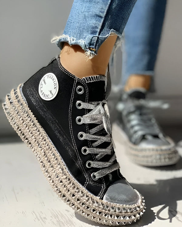 Une image d'une paire de chaussures montantes noires avec des lacets argentés. Les chaussures sont portées par une femme qui porte des jeans bleus déchirés.