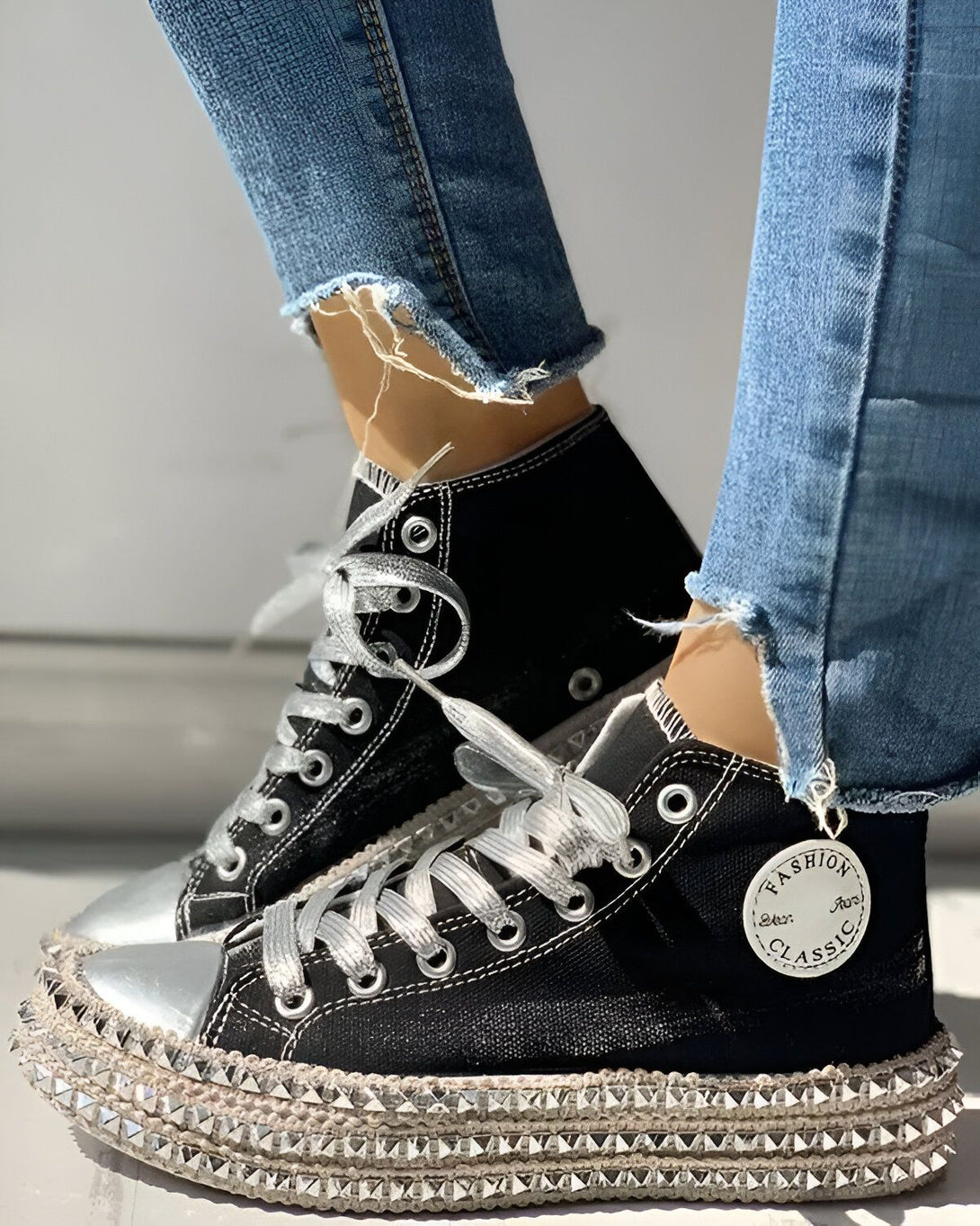 Une image d'une paire de chaussures montantes noires avec des lacets argentés et une semelle compensée. Les chaussures sont portées avec un jean bleu troué.