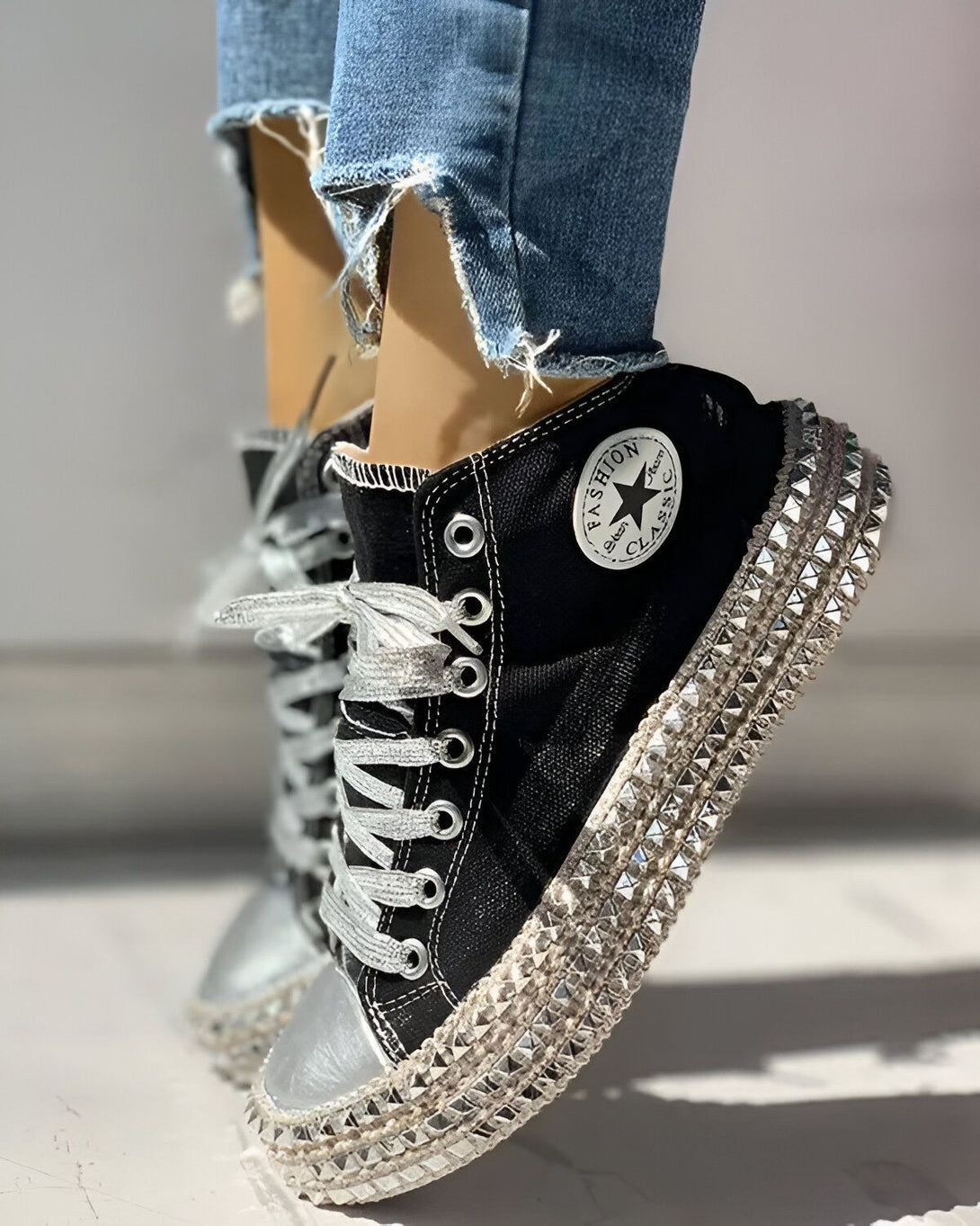 Une image d'une paire de chaussures montantes noires avec des lacets argentés et des clous argentés sur la semelle.