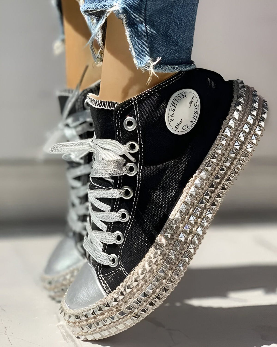 Une image d'une paire de sneakers noires avec des lacets argentés et des clous argentés sur la semelle.