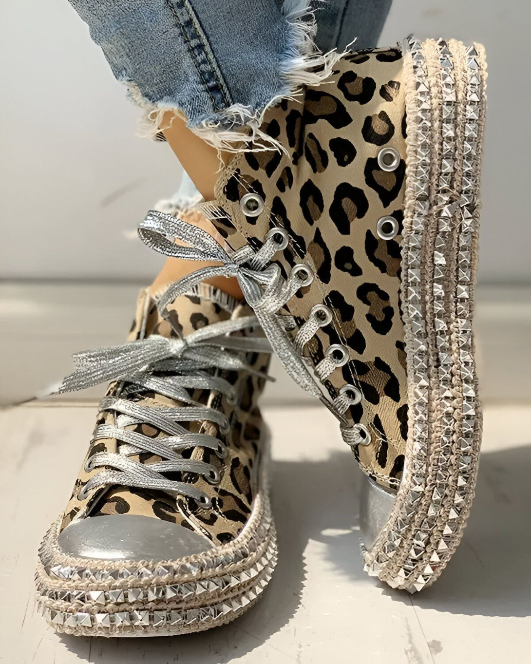 Une paire de sneakers montantes à lacets, à bout rond et à semelle compensée. Les sneakers sont de couleur marron et à motif léopard, avec des clous argentés sur la semelle et le talon.