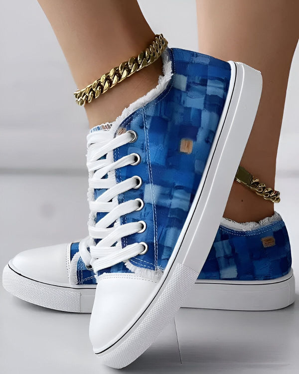 Une paire de baskets basses bleues et blanches avec des lacets blancs. Les baskets sont portées par une femme qui porte également une chaîne de cheville en or.