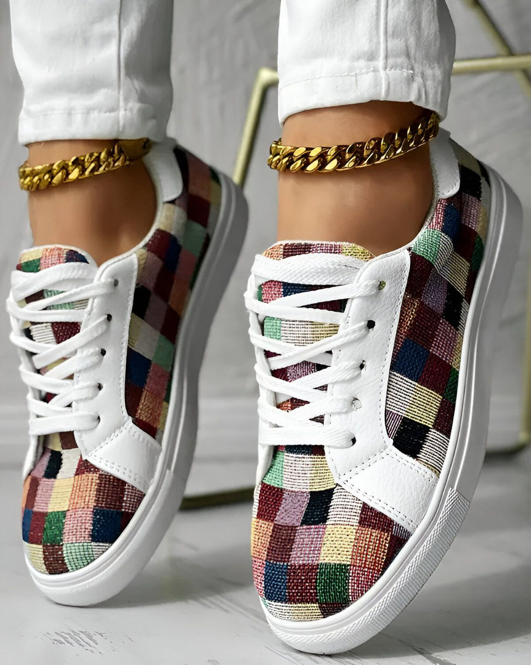 Une femme porte des baskets colorées avec un pantalon blanc et des bijoux en or.