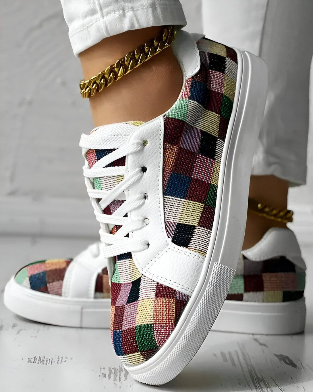 Une femme porte des baskets basses multicolores à lacets avec une semelle blanche. Elle porte également un jean blanc et un bracelet de cheville doré.