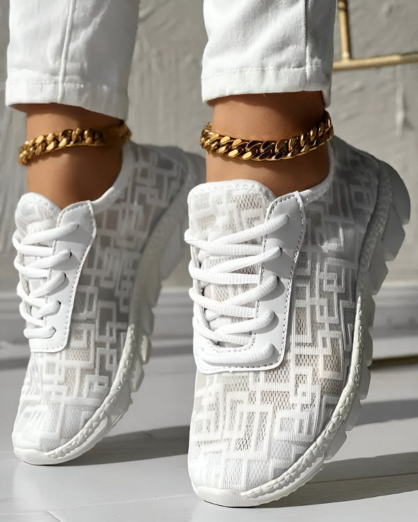 Une femme porte des baskets blanches avec des lacets blancs et des semelles blanches. Elle porte également un pantalon blanc et des chaussettes blanches. Les baskets sont en maille et ont un motif de carrés. La femme est debout sur un sol en béton.