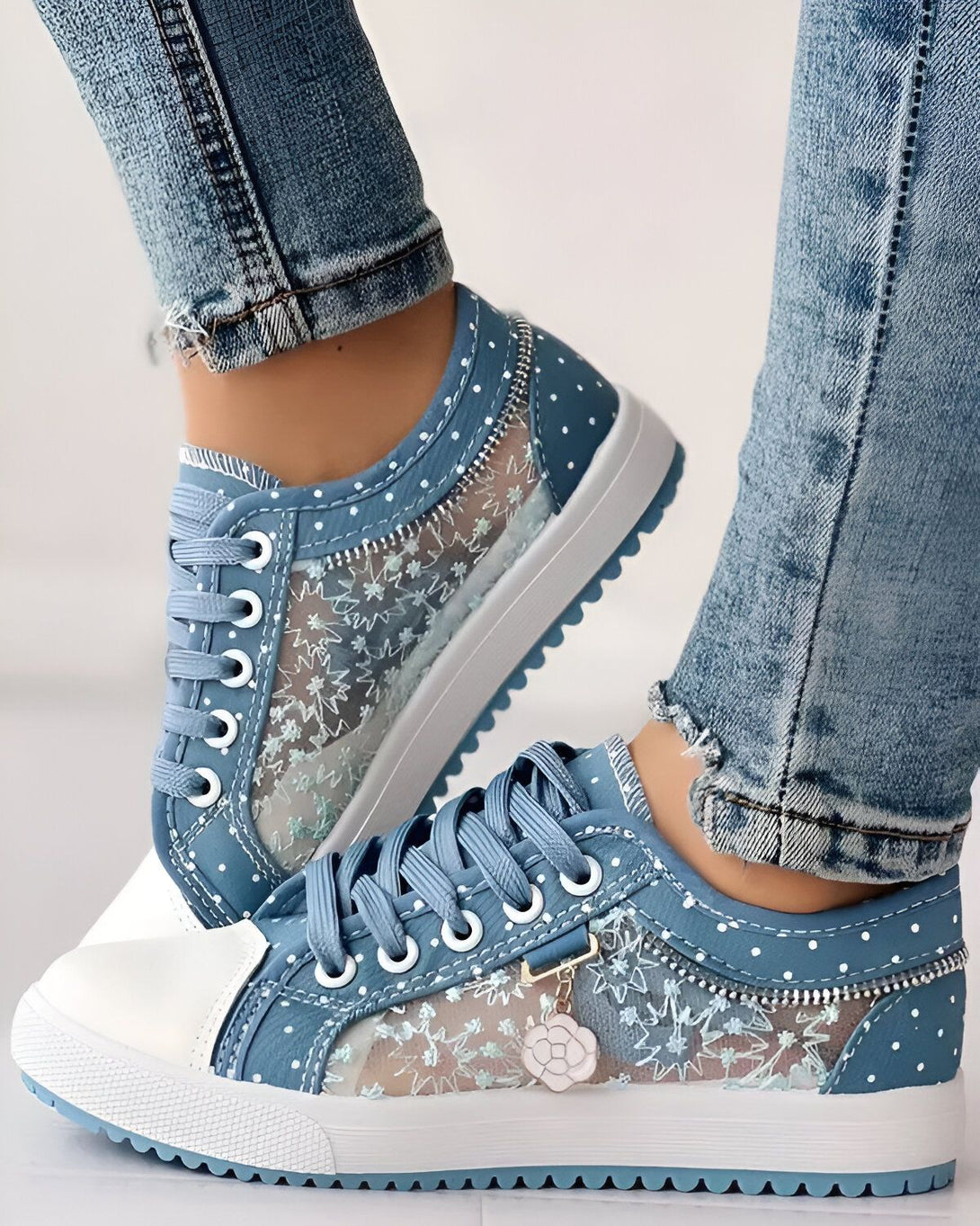 Une image d'une paire de chaussures de sport bleues et blanches avec un motif floral. Les chaussures sont portées par une femme qui porte un jean bleu.