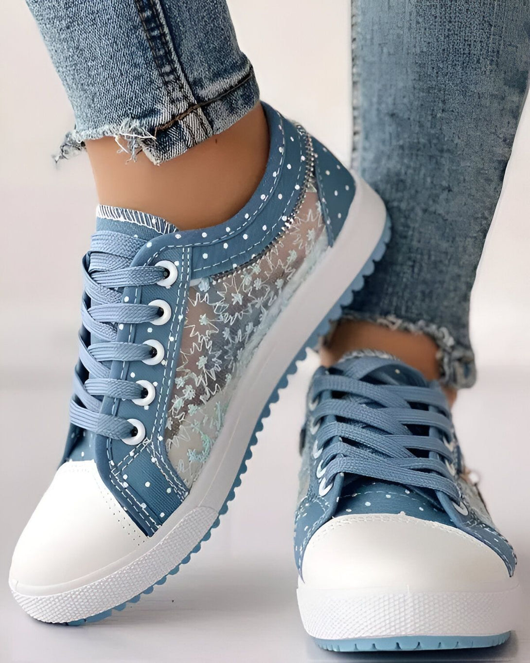 Une paire de chaussures basses bleues avec des lacets blancs et une semelle blanche. Les chaussures sont en toile et ont un motif de pois blancs.