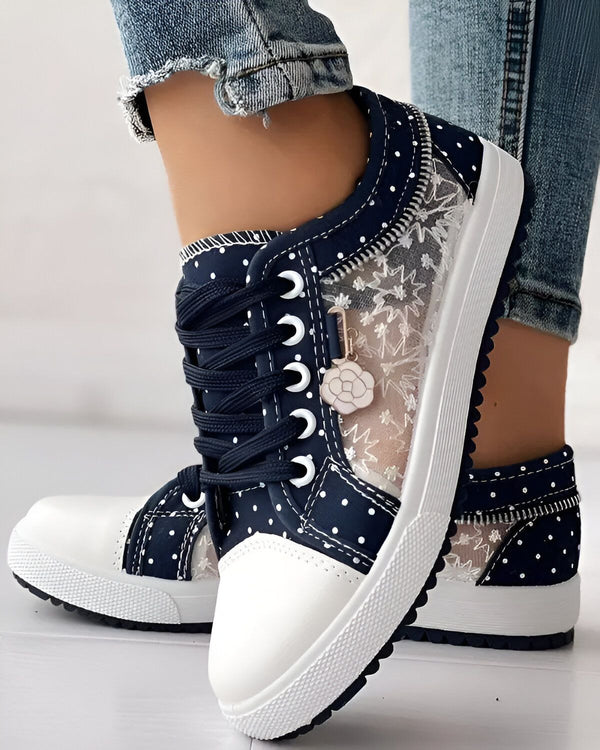 Une paire de chaussures basses bleues à pois blancs avec des lacets et une fermeture éclair sur le côté. Les chaussures sont portées par une femme qui porte un jean bleu.
