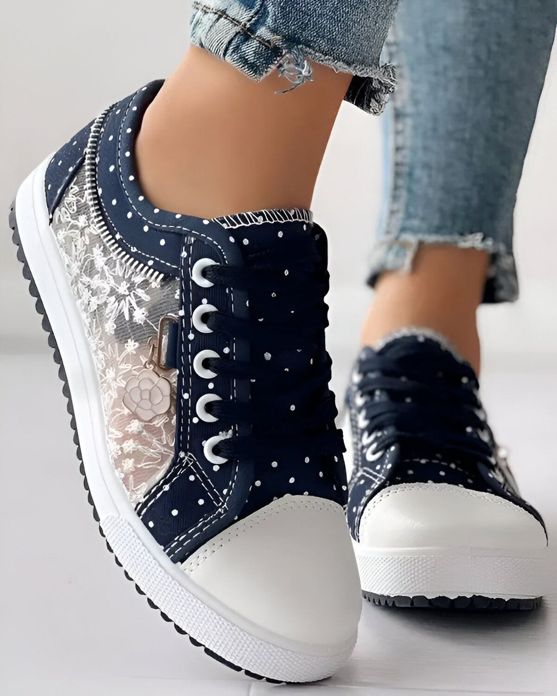 Une paire de baskets basses bleues avec des pois blancs et des lacets blancs. Les baskets sont en toile et ont une semelle blanche.