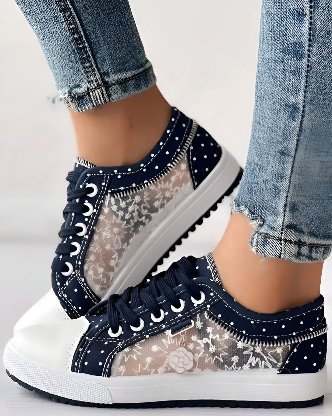 Une femme porte des baskets bleues et blanches avec des lacets et une semelle blanche. Les baskets sont en toile et ont un motif floral.