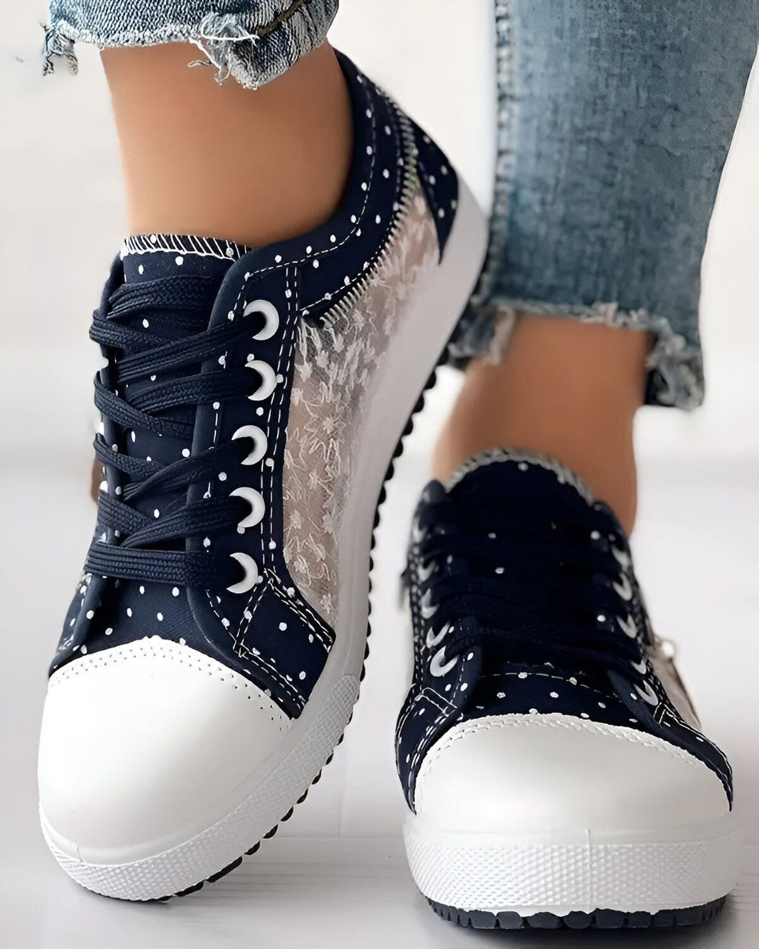 Une paire de chaussures basses bleues avec des pois blancs et des lacets blancs. Les chaussures sont portées par une femme qui porte des jeans bleus.