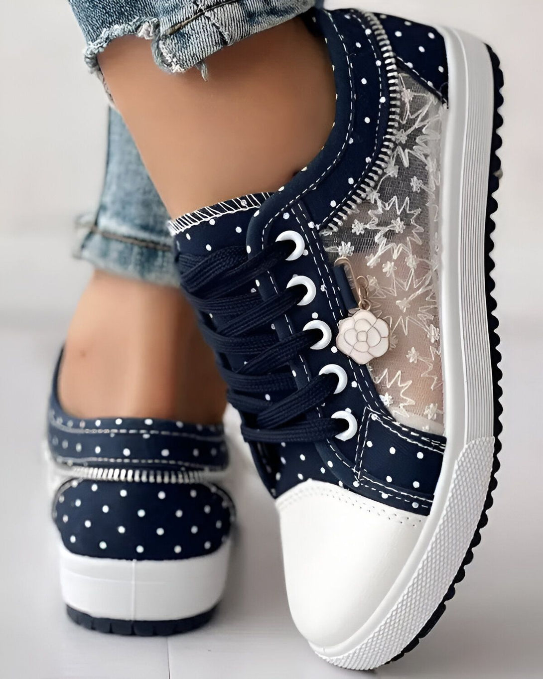 Une image d'une paire de chaussures bleues à pois blancs avec des lacets noirs et une fermeture éclair sur le côté. Les chaussures sont portées par une femme qui porte des jeans bleus.