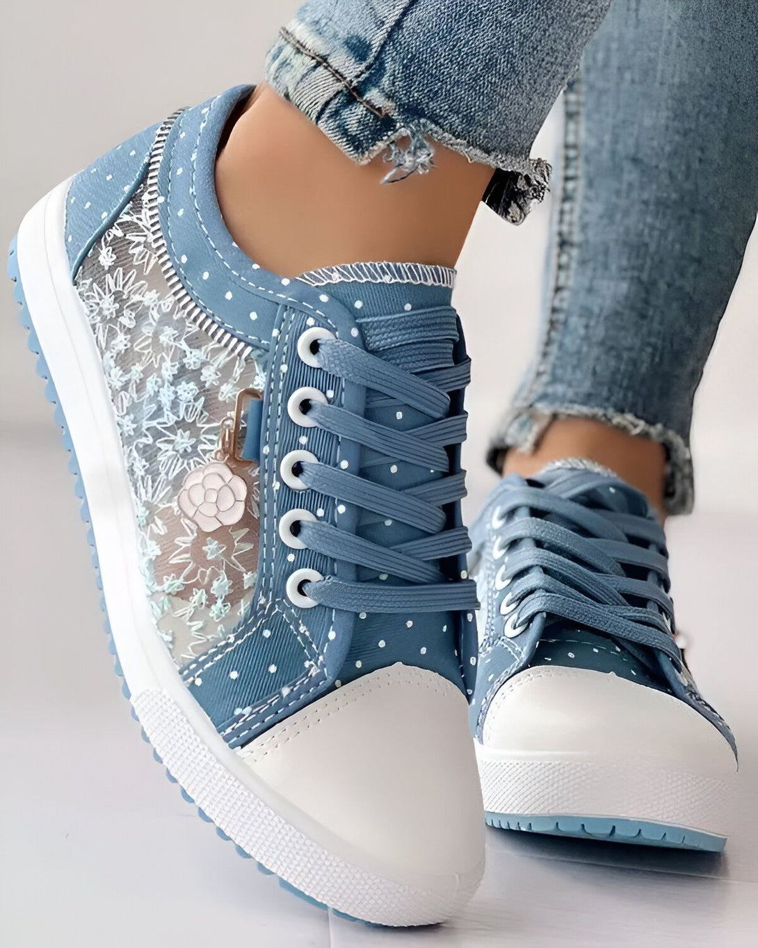 Une paire de chaussures basses bleues avec des lacets blancs et une semelle blanche. Les chaussures sont en toile et ont un motif floral.