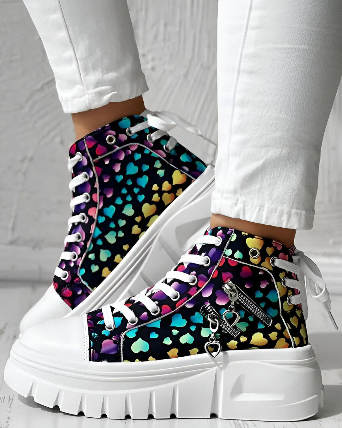 Une paire de chaussures montantes à lacets avec un motif de cœurs multicolores sur fond noir. Les semelles sont blanches.