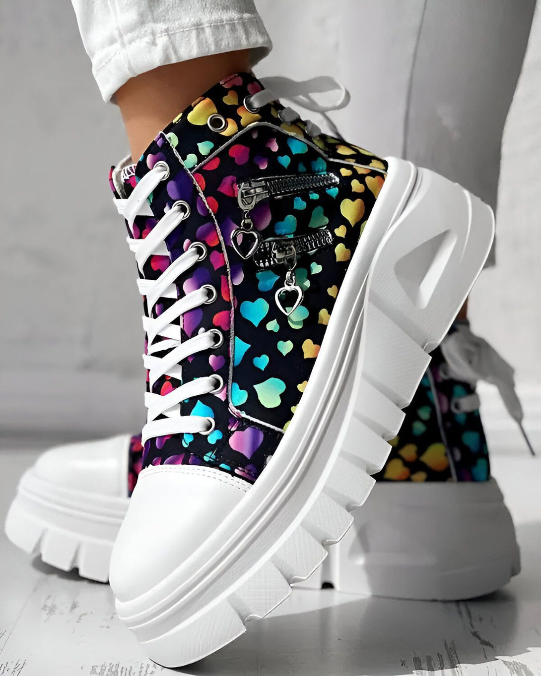 Une paire de chaussures montantes à lacets avec une plateforme blanche et une tige imprimée de cœurs multicolores.