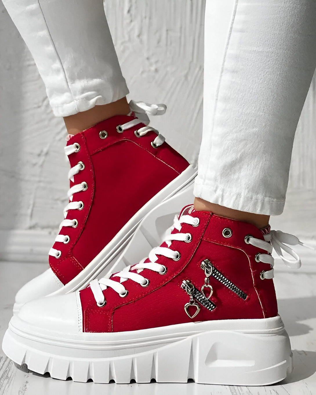Une paire de chaussures montantes rouges avec un zip sur le côté et un lacet rouge. La semelle est blanche et épaisse.