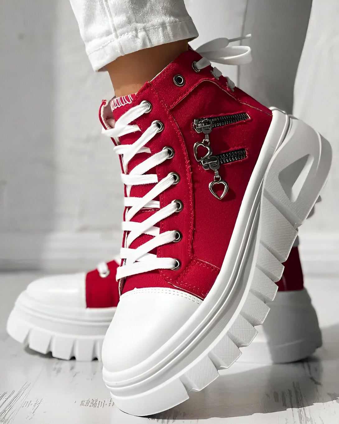 Une paire de bottes rouges à lacets avec une fermeture éclair sur le côté. Les bottes ont une semelle blanche épaisse et une tige en toile rouge.