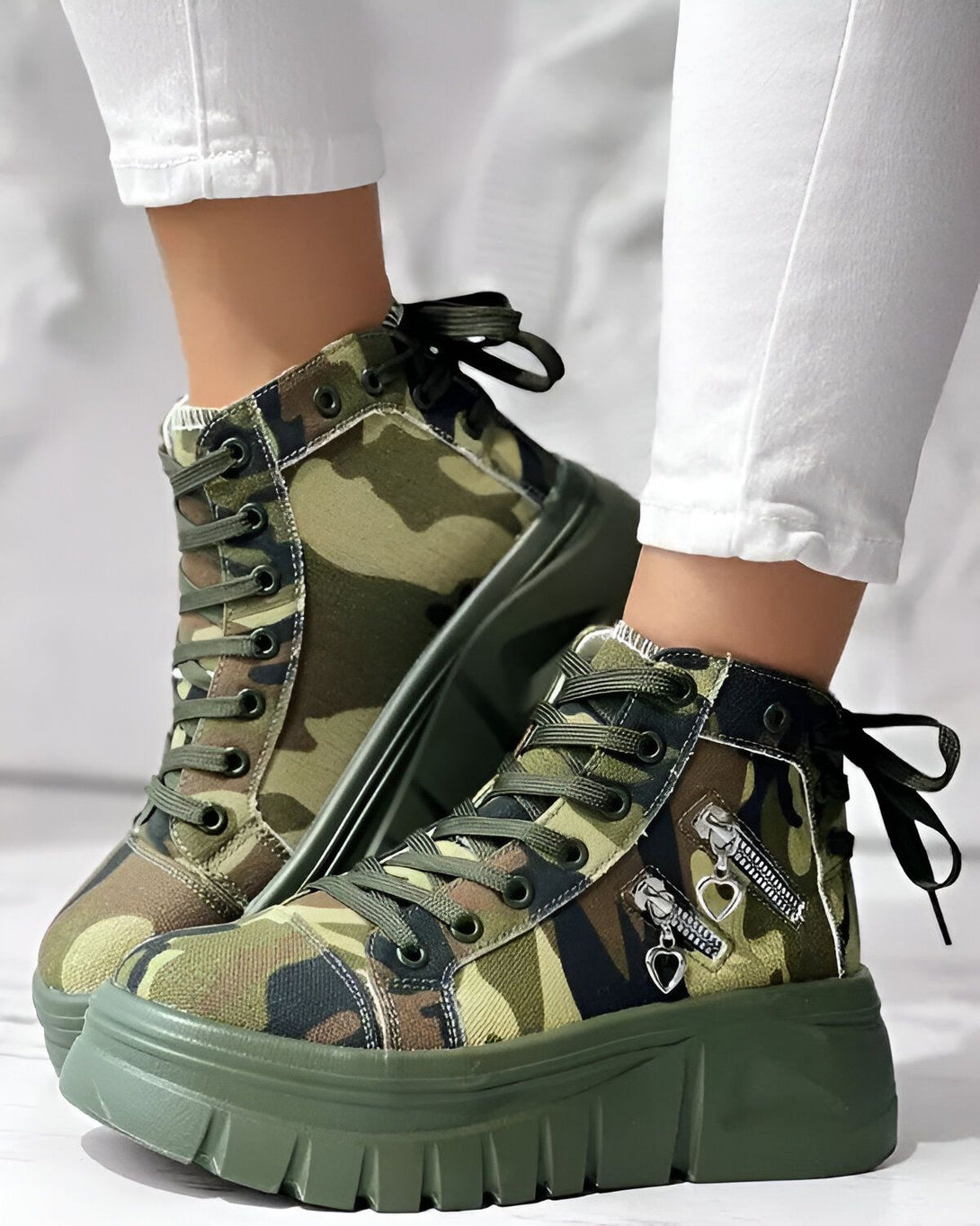 Une paire de bottes à lacets montantes à plateforme à motif camouflage vert avec un zip sur le côté.