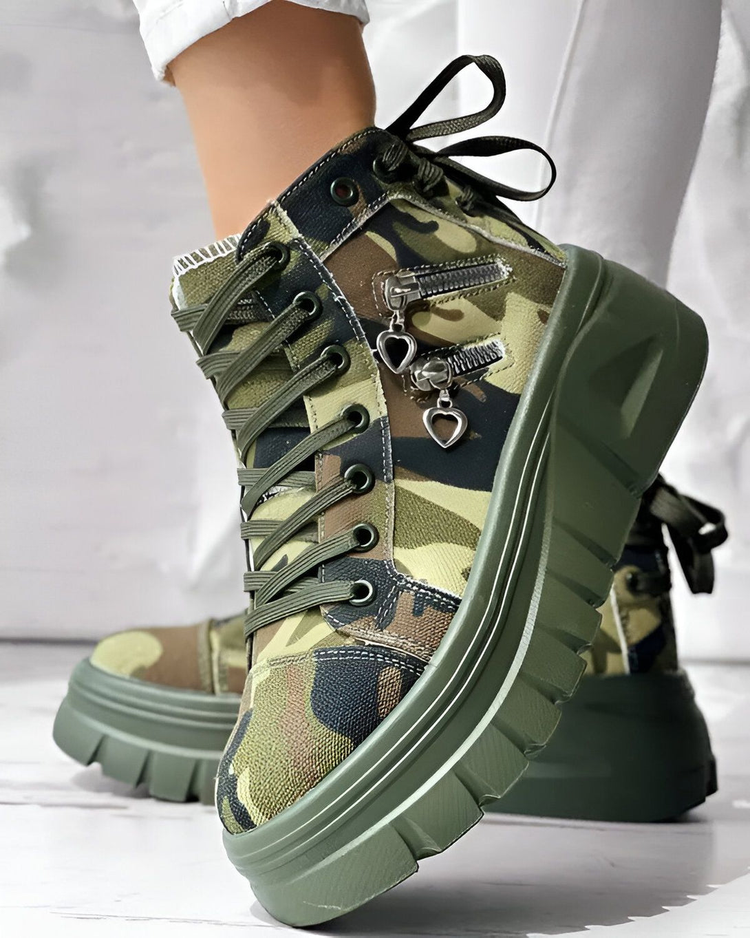 Une paire de bottes militaires à plateforme verte avec un motif camouflage et des lacets. Les bottes ont une fermeture éclair sur le côté et un cœur en métal sur le devant.