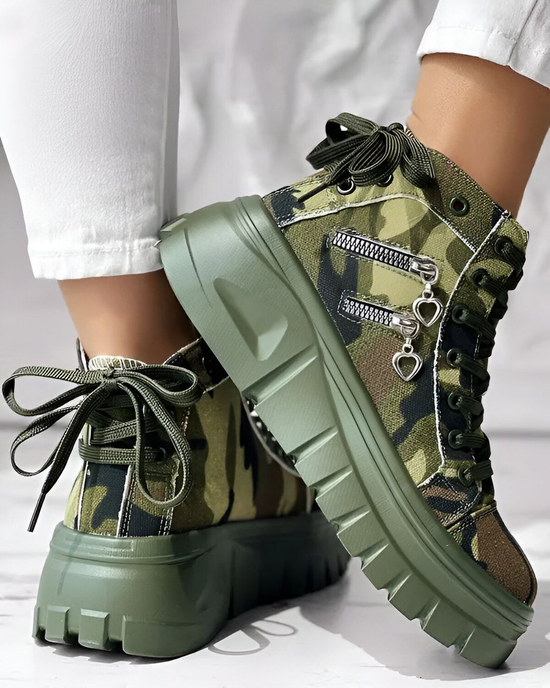 Une paire de bottes à plateforme verte avec un motif camouflage. Les bottes sont lacées et ont une fermeture éclair sur le côté.