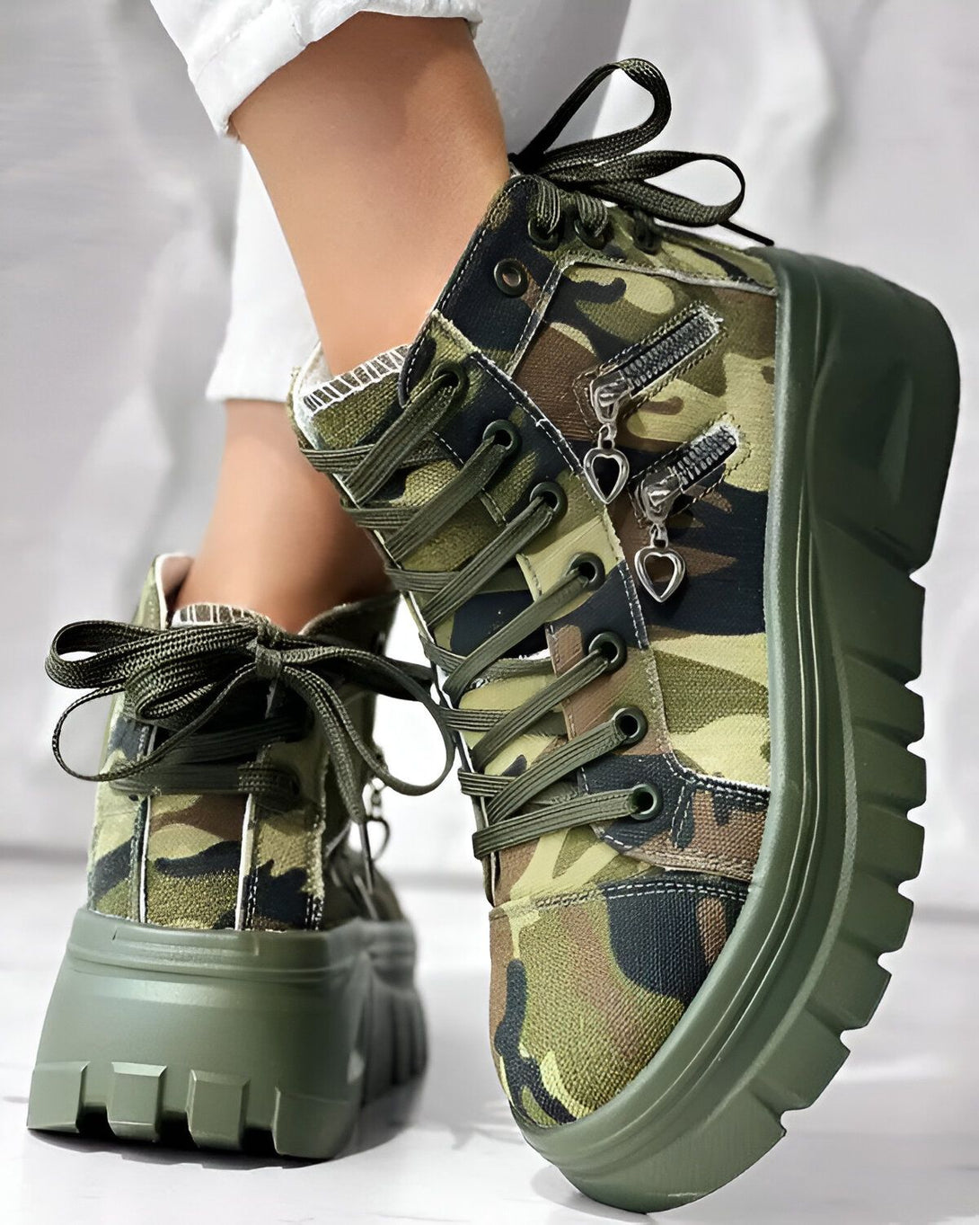Une paire de bottes à plateforme verte et marron avec un motif camouflage. Les bottes sont lacées et ont une fermeture éclair sur le côté.
