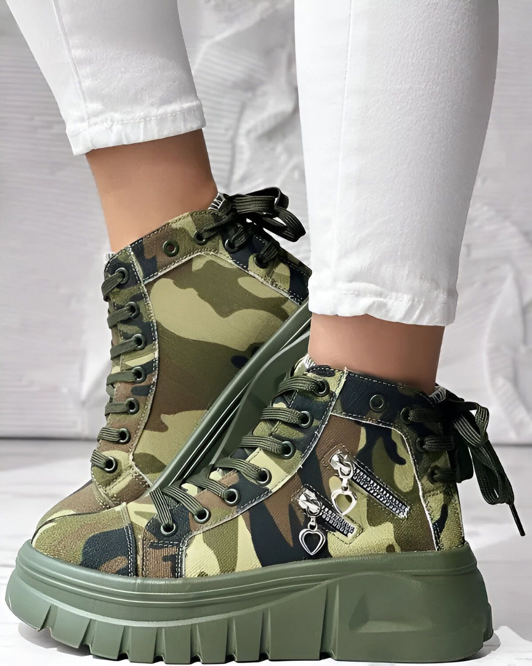 Une paire de bottes militaires à lacets, à plateforme et à fermeture éclair sur le côté. Les bottes sont de couleur kaki et ont un motif camouflage.