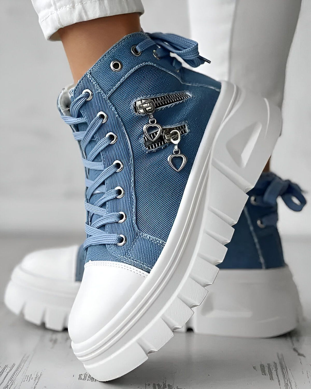 Une image d'une paire de bottines compensées en jean bleu avec des lacets et une fermeture éclair sur le côté. Les semelles sont blanches et crantées.