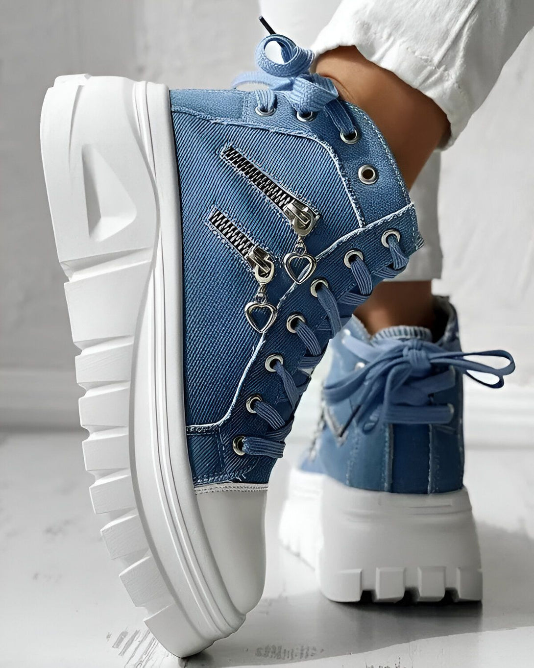 Une paire de bottes montantes en jean bleu avec des lacets et une fermeture éclair sur le côté. Les semelles sont blanches et épaisses.