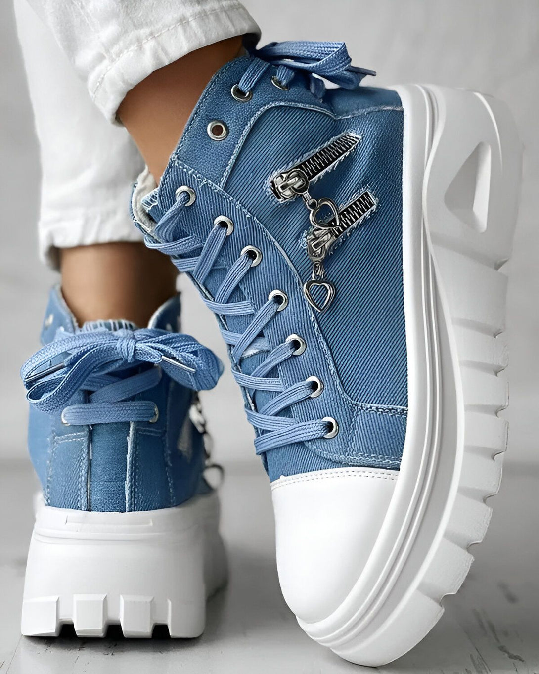 Une paire de chaussures montantes en jean bleu avec des lacets et une fermeture éclair sur le côté. Les semelles sont blanches et épaisses.