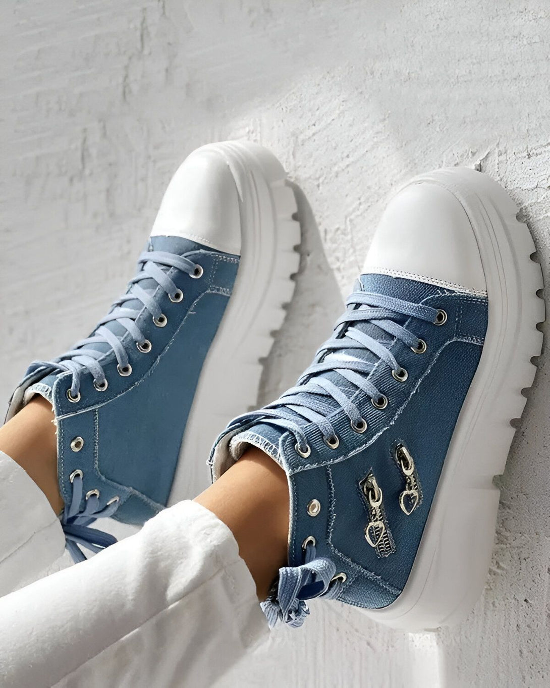 Une paire de chaussures montantes en jean bleu avec des lacets et une fermeture éclair sur le côté. Les semelles sont blanches et épaisses.