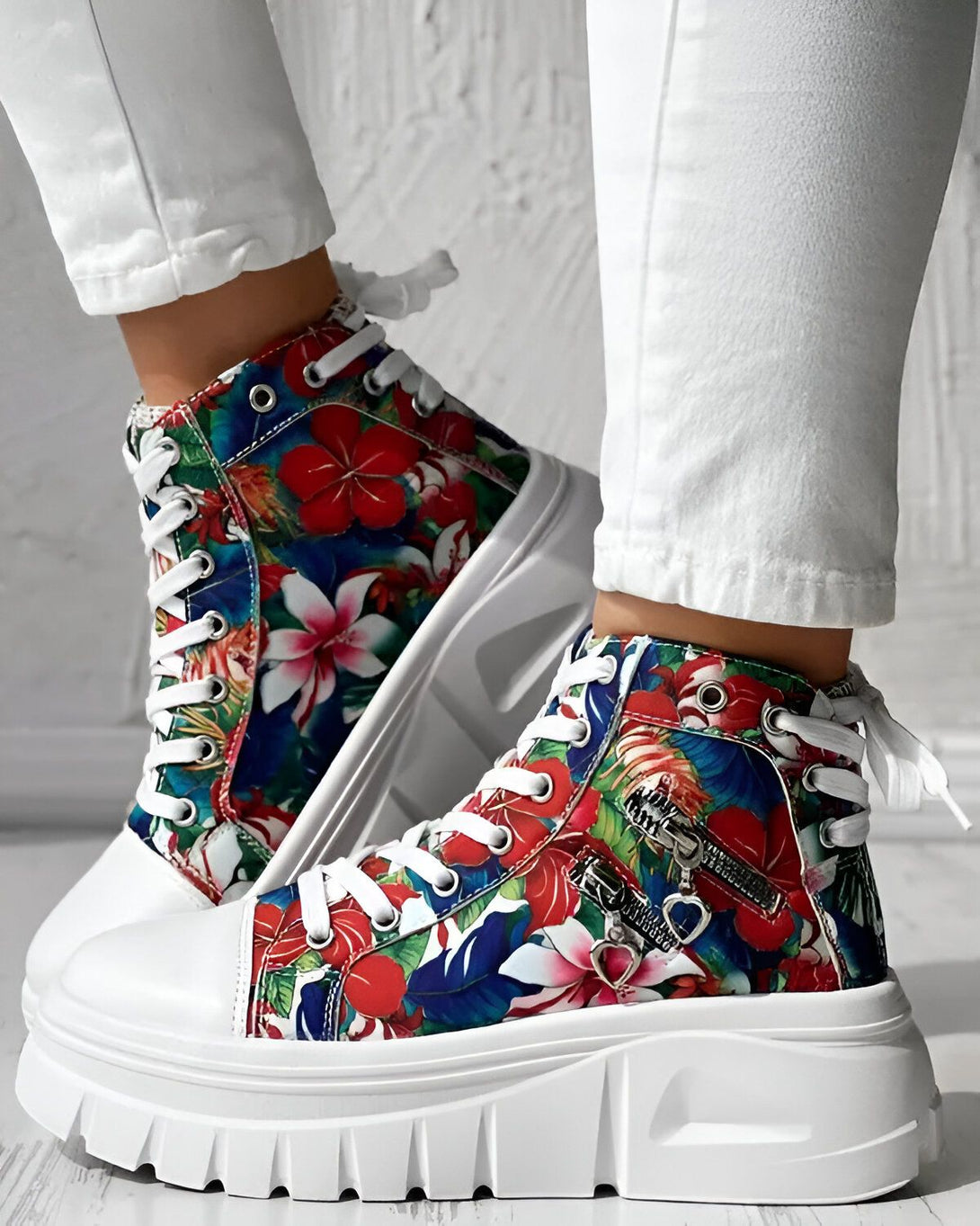 Une femme porte des baskets montantes à lacets. Les baskets sont blanches avec un imprimé floral coloré. La femme porte un jean blanc et les baskets sont assorties à son jean.