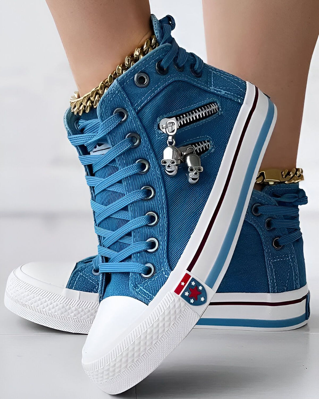 Une paire de sneakers montantes bleues avec des lacets blancs et une fermeture éclair sur le côté. Il y a un pendentif en forme de tête de mort sur la fermeture éclair. Les semelles sont blanches.