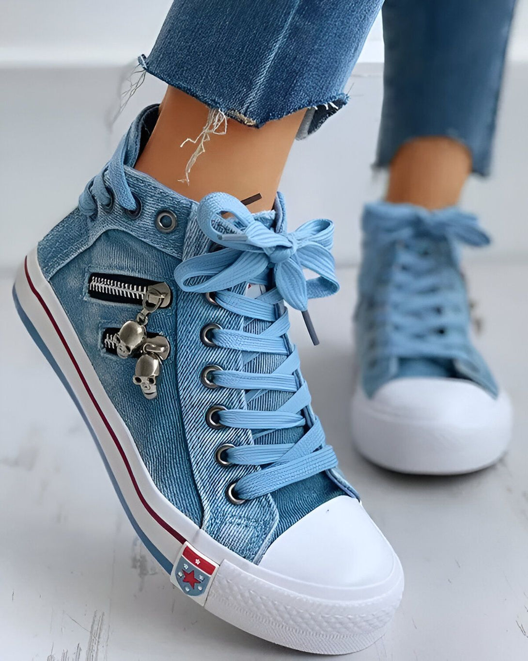 Une image d'une paire de chaussures montantes en toile bleue avec des lacets bleus et une fermeture éclair sur le côté. Il y a un pendentif en forme de tête de mort sur la fermeture éclair. Les chaussures sont portées par une femme qui porte un jean bleu troué.