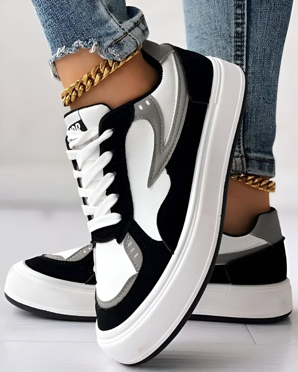 Une paire de baskets noires et blanches avec des lacets blancs et une semelle épaisse. Les baskets sont portées par une femme qui porte un jean bleu et un chemisier blanc.